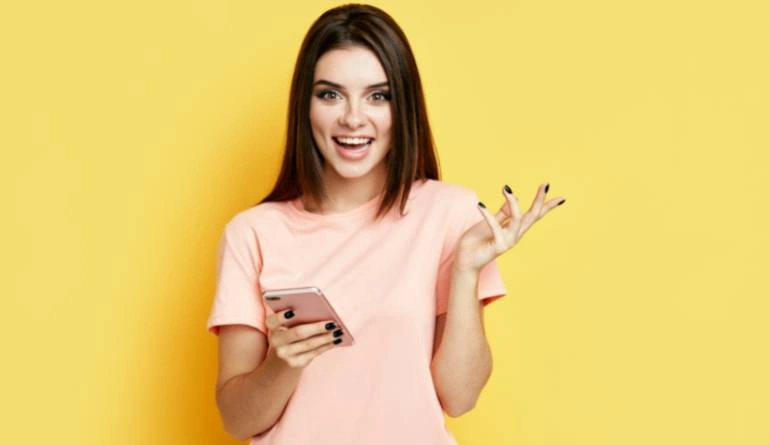 Χαρούμενη κοπέλα κρατάει κινητό τηλέφωνο σε κίτρινο φόντο