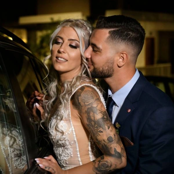 Νύφη με λευκό νυφικό και γαμπρός με μπλε κοστούμι αγκαλιάζονται τρυφερά.