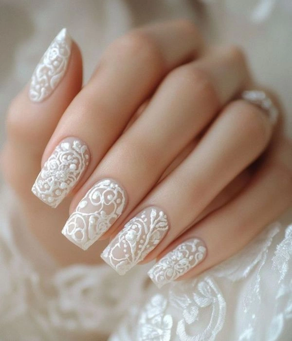 Νυφικά νύχια με σχέδια δαντέλας σε λευκό χρώμα, σε τετράγωνο σχήμα, που ταιριάζουν με το δαντελένιο νυφικό φόρεμα.