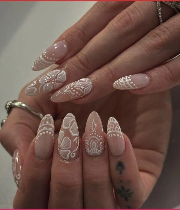 Νυφικά νύχια με σχέδια δαντέλας σε λευκό χρώμα, πάνω σε nude βάση, σε σχήμα αμυγδάλου.