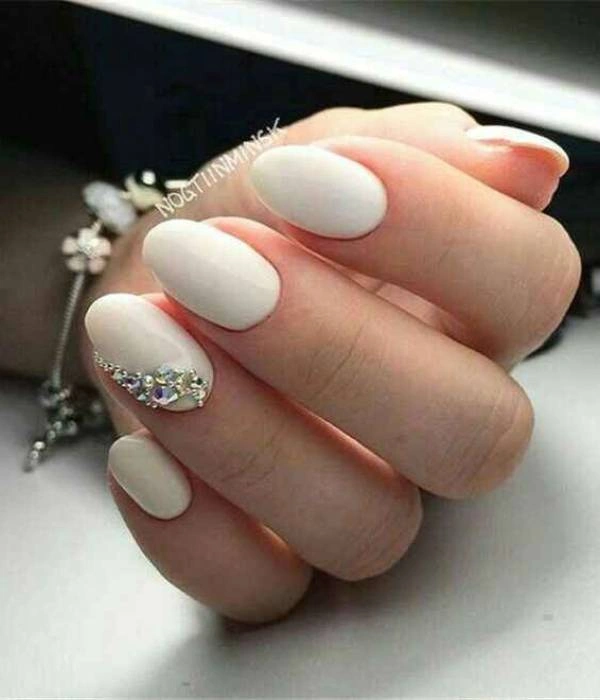 Λευκά νυφικά νύχια με στρας σε οβάλ σχήμα, διακοσμημένα με ένα ασημένιο βραχιόλι.