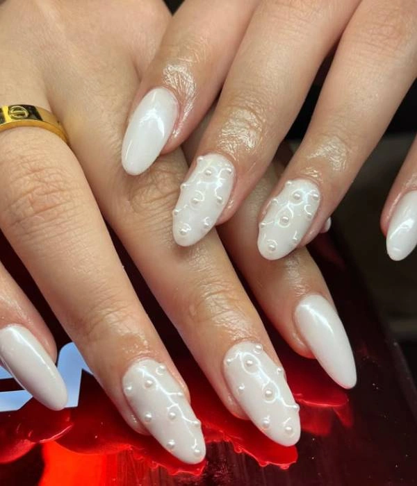 Νυφικά νύχια με μαργαριτάρια σε λευκή βάση, σε αμυγδαλωτό σχήμα, με ένα χρυσό δαχτυλίδι Cartier Love.