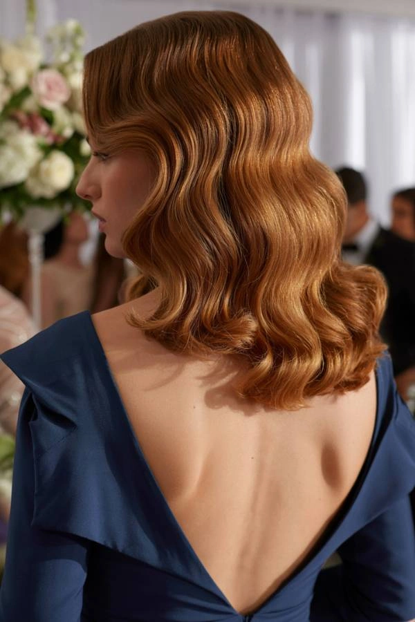 Κομψό χτένισμα κουμπάρας: Πίσω όψη με καλοσχηματισμένες κλασικές Hollywood waves σε μεσαίου μήκους μαλλιά.