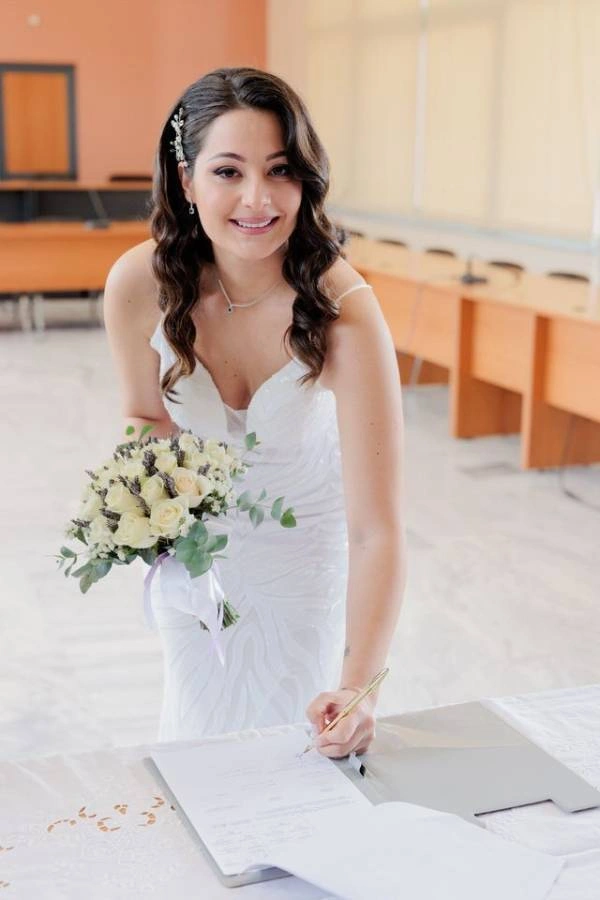 Φωτογραφία νύφης που υπογράφει τα έγγραφα του πολιτικού της γάμου, κρατώντας ανθοδέσμη.