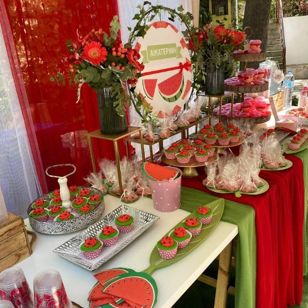 Καλοκαιρινός στολισμός βάπτισης με θέμα το καρπούζι, σε αποχρώσεις κόκκινου, πράσινου και λευκού, με γλυκά, υφάσματα και διακοσμητικά εμπνευσμένα από φρούτα.
