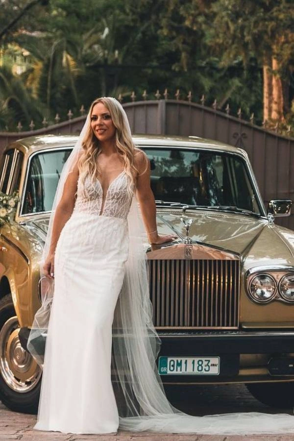 Νύφη με λευκό νυφικό στέκεται μπροστά σε χρυσό κλασικό Rolls Royce διακοσμημένο με λουλούδια