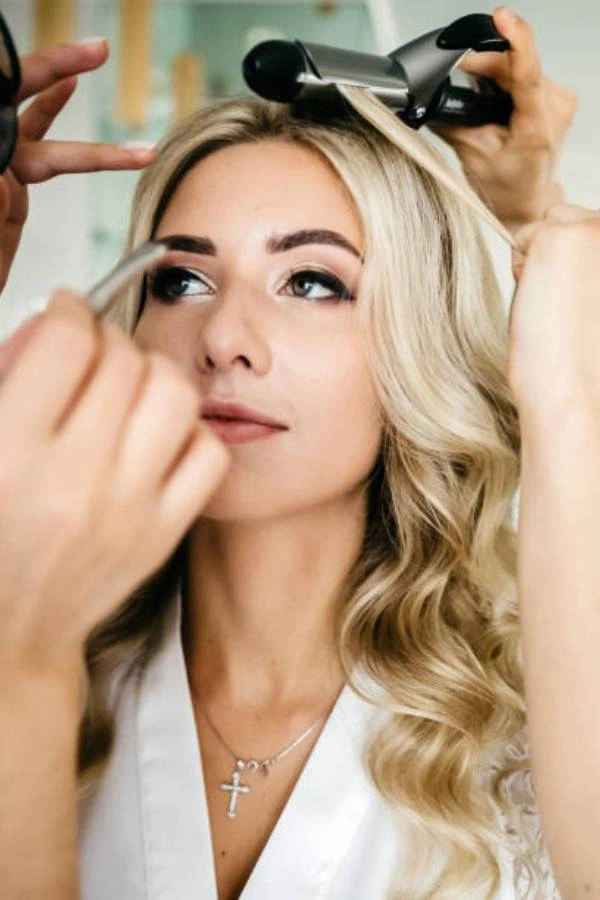 Νύφη με ξανθά μαλλιά σε διαδικασία μακιγιάζ και hairstyling