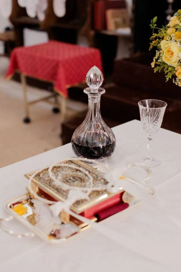 Σετ γάμου με επάργυρο δίσκο, καράφα με κόκκινο κρασί, ποτήρι και στέφανα πάνω σε τραπέζι εκκλησίας