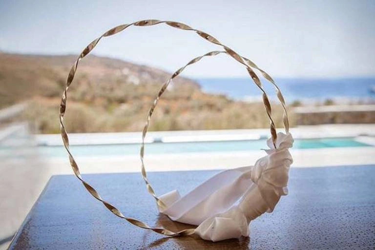 Στέφανα γάμου τοποθετημένα σε ξύλινη επιφάνεια με φόντο τη θάλασσα και το ελληνικό τοπίο