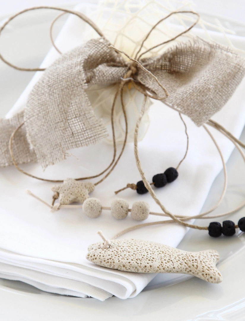 Μπομπονιέρα γάμου σε λευκή πετσέτα με φυσικά υλικά, λινό φιόγκο και χειροποίητα διακοσμητικά σε μορφή ψαριού, από τη Vassiliki Creations