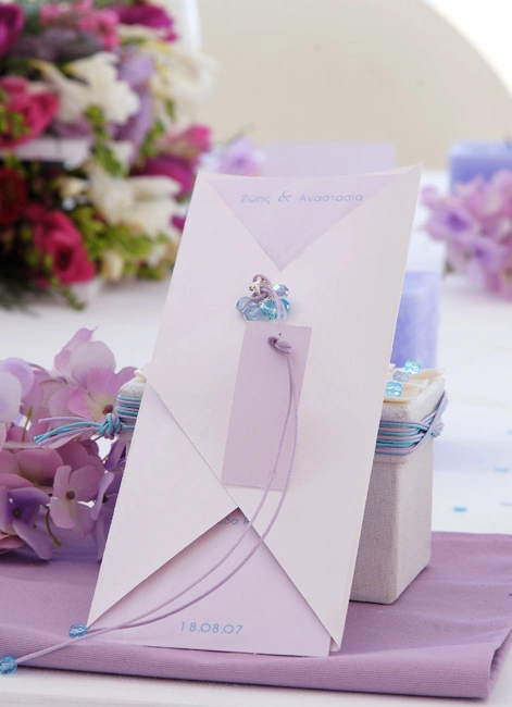 Παστέλ προσκλητήριο γάμου σε λιλά απόχρωση με διακοσμητικό κορδόνι και χάντρες, σε στολισμένο τραπέζι από τη Vassiliki Creations