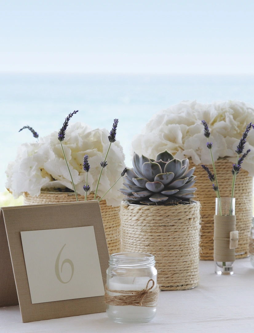 Boho διακόσμηση τραπεζιού γάμου με λευκά άνθη, λεβάντα και παχύφυτα σε νησιώτικο σκηνικό δίπλα στη θάλασσα, από τη Vassiliki Creations