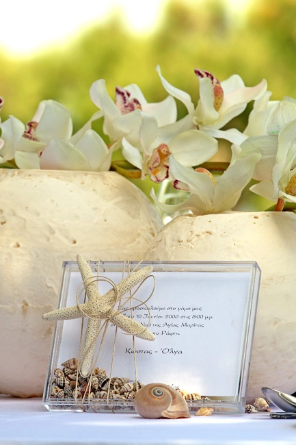Καλοκαιρινό προσκλητήριο γάμου με διακόσμηση από αστερία, κοχύλια και λευκές ορχιδέες, σε παραθαλάσσιο στολισμό από τη Vassiliki Creations