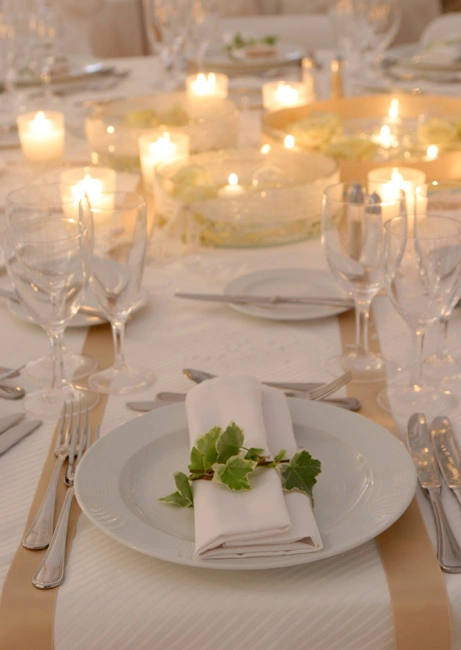 Ρομαντικός στολισμός τραπεζιού γάμου με λευκά κεριά, χρυσές λεπτομέρειες και φύλλα πρασινάδας σε elegant σερβίρισμα, από τη Vassiliki Creations