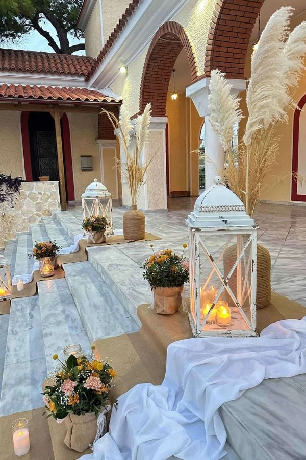 Boho στολισμός εκκλησίας με pampas grass, φανάρια, λινά υφάσματα και λουλούδια σε γήινους τόνους, δημιουργώντας φυσική και ρομαντική ατμόσφαιρα.