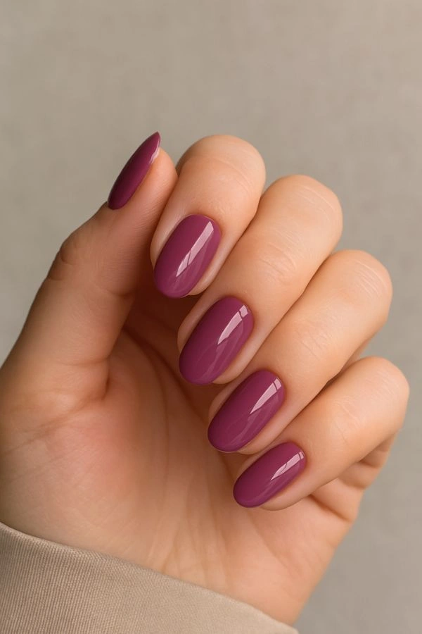 Κοντινό σε χέρι καλεσμένης με γυαλιστερό mauve μανικιούρ σε ουδέτερο φόντο, κομψή επιλογή για νύχια για γάμο.