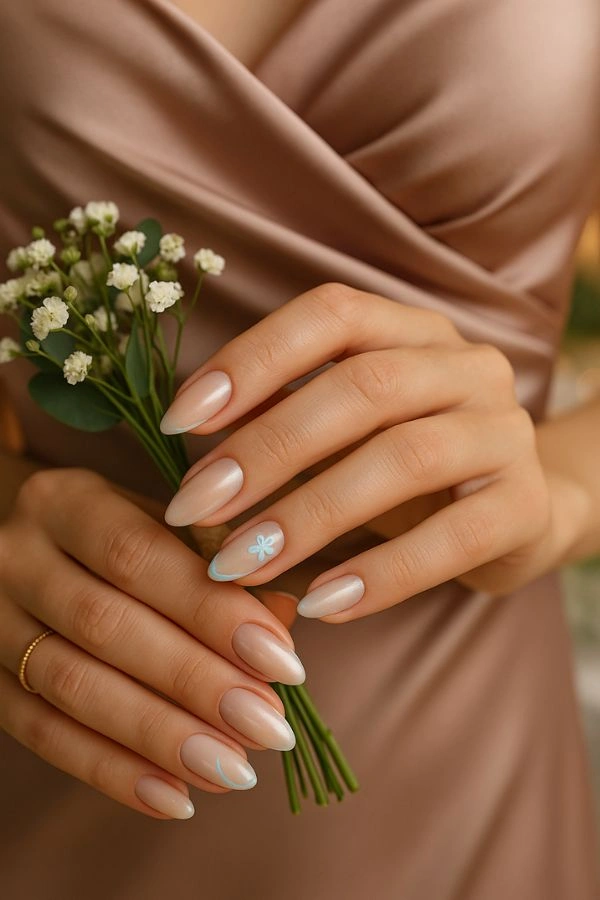 Νύχια για γάμο κουμπάρα σε μεσαίο almond μήκος με nude βάση και διακριτικό chrome, λεπτή baby blue γραμμή και μικρό λουλουδάκι, κοντινό πλάνο με σατινέ φόρεμα και ανθοδέσμη.