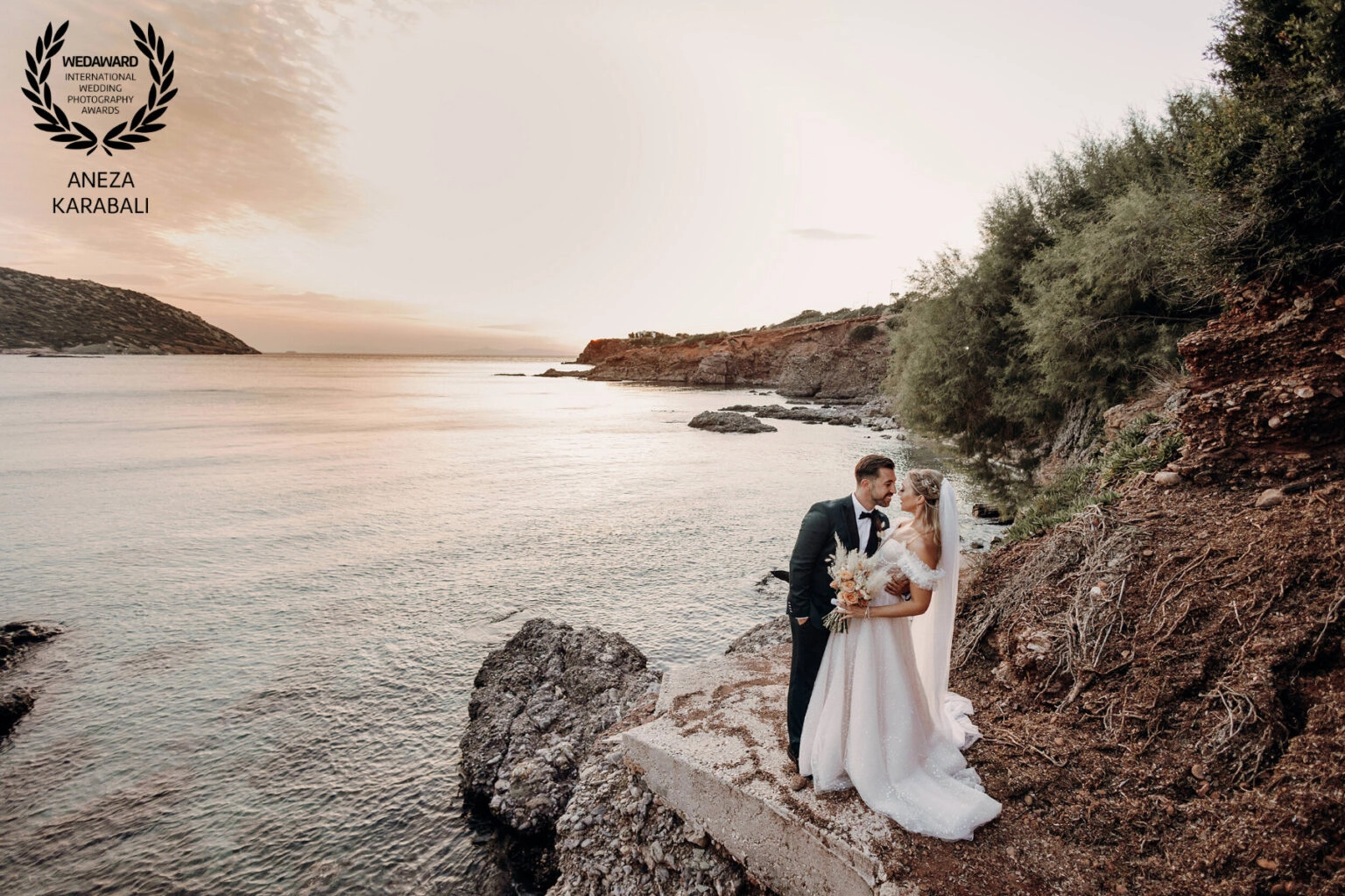 Ζευγάρι αγκαλιασμένο σε βραχώδη ακτή κατά τη δύση του ήλιου