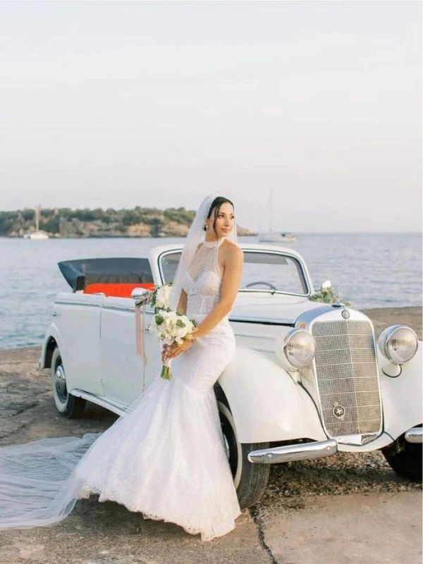 Νύφη δίπλα σε κλασικό cabrio αυτοκίνητο γάμου με φόντο τη θάλασσα