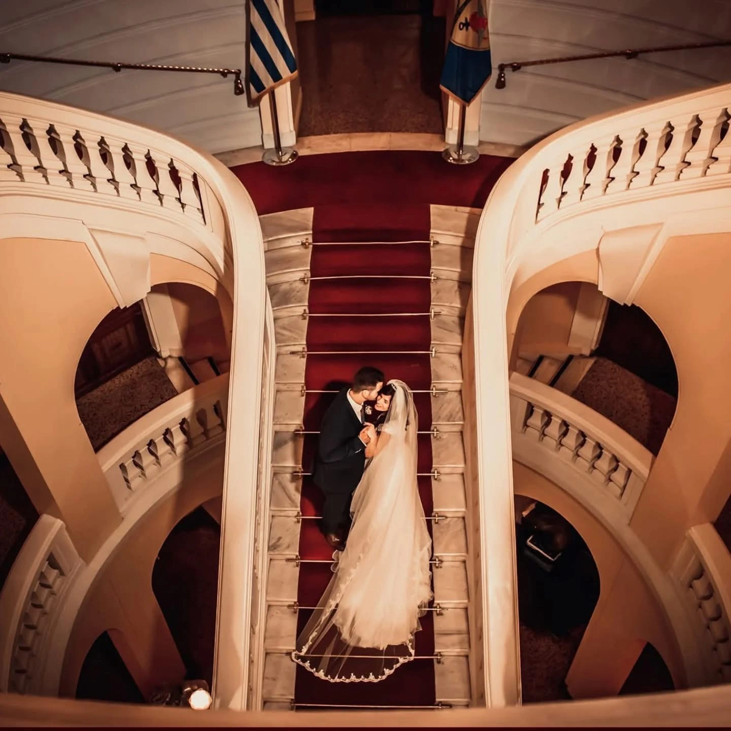 Ζευγάρι σε εντυπωσιακή σκάλα με κόκκινο χαλί σε καλλιτεχνική φωτογράφιση γάμου από την Wedding Stars